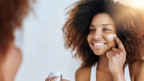Shot of an attractive young woman applying moisturizer to her face in front of the mirror